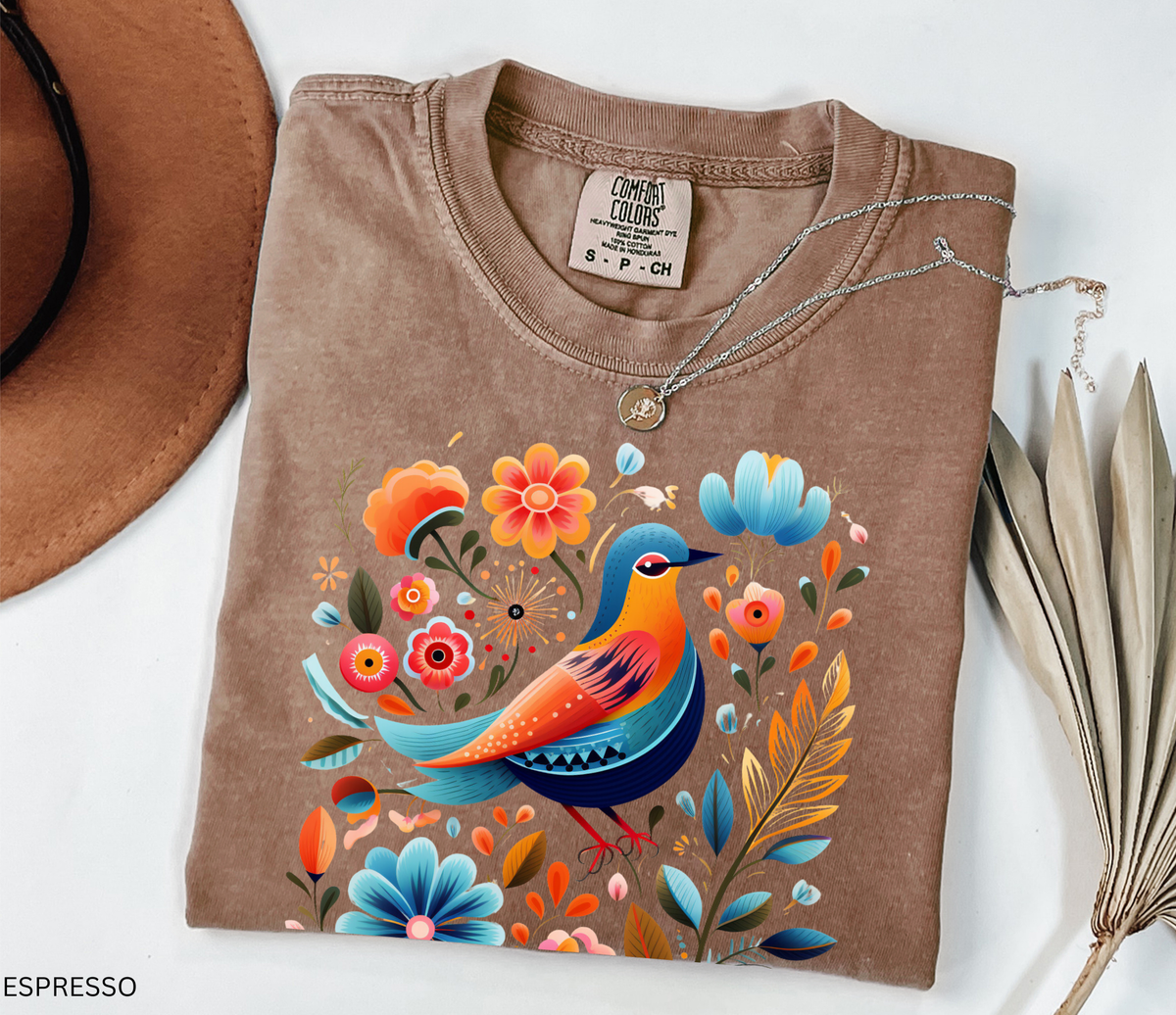 Colorful Nordic folk art bird graphic t-shirt featuring bright flowers, leaves, and botanical details.