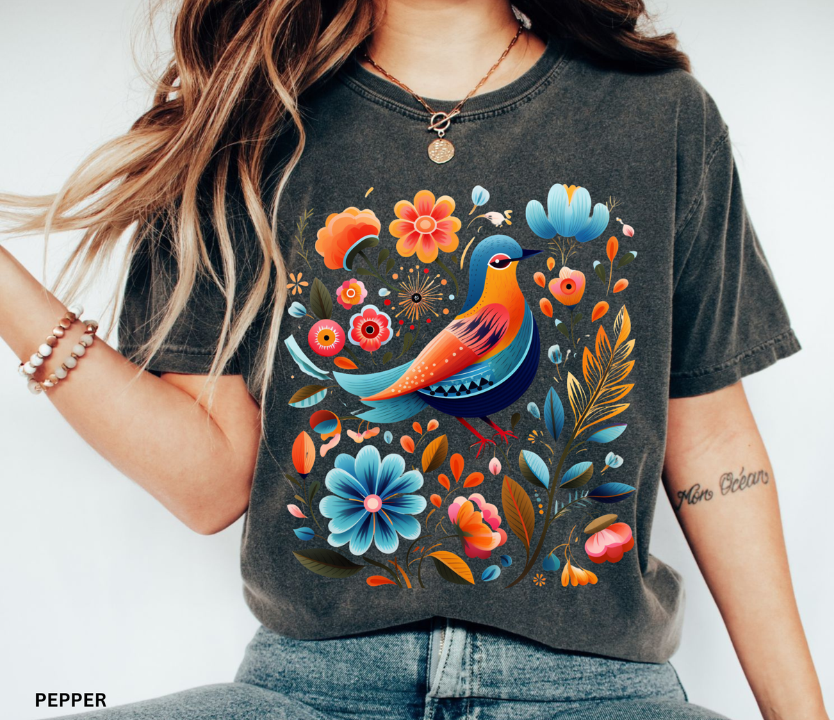 A woman wearing a dark charcoal gray graphic t-shirt with a colorful illustration of a bird and flowers. The text 'PEPPER' is visible in the bottom-left corner.