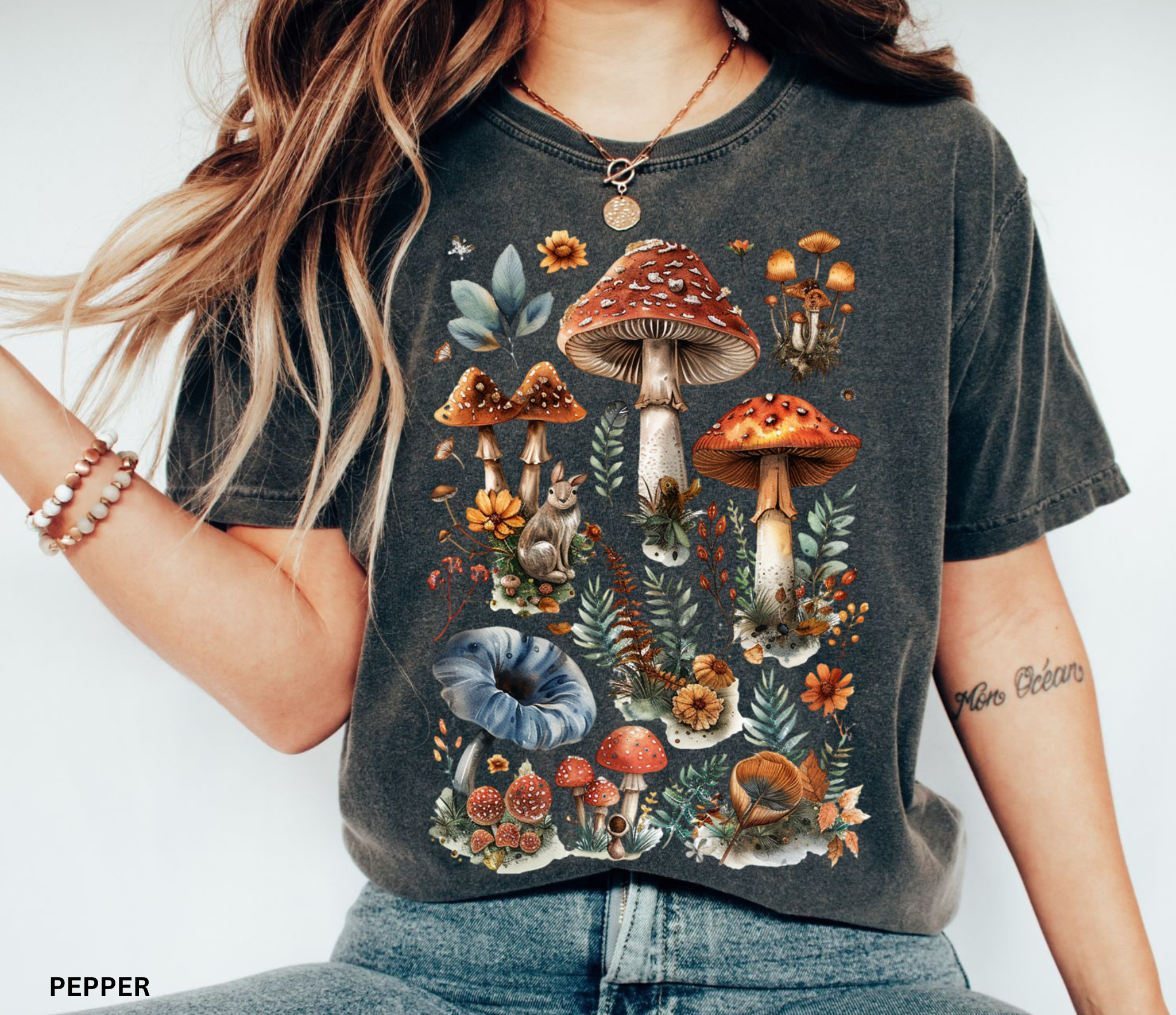 Illustrated woodland collage featuring red and brown mushrooms, leaves, flowers, and forest details in a vintage watercolor style, printed on a Comfort Colors shirt.