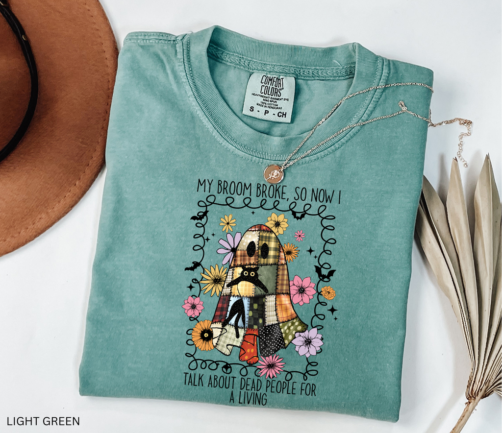 Halloween shirt with a patchwork quilt ghost holding a black cat, surrounded by colorful flowers. Cute cozy spooky season tee.