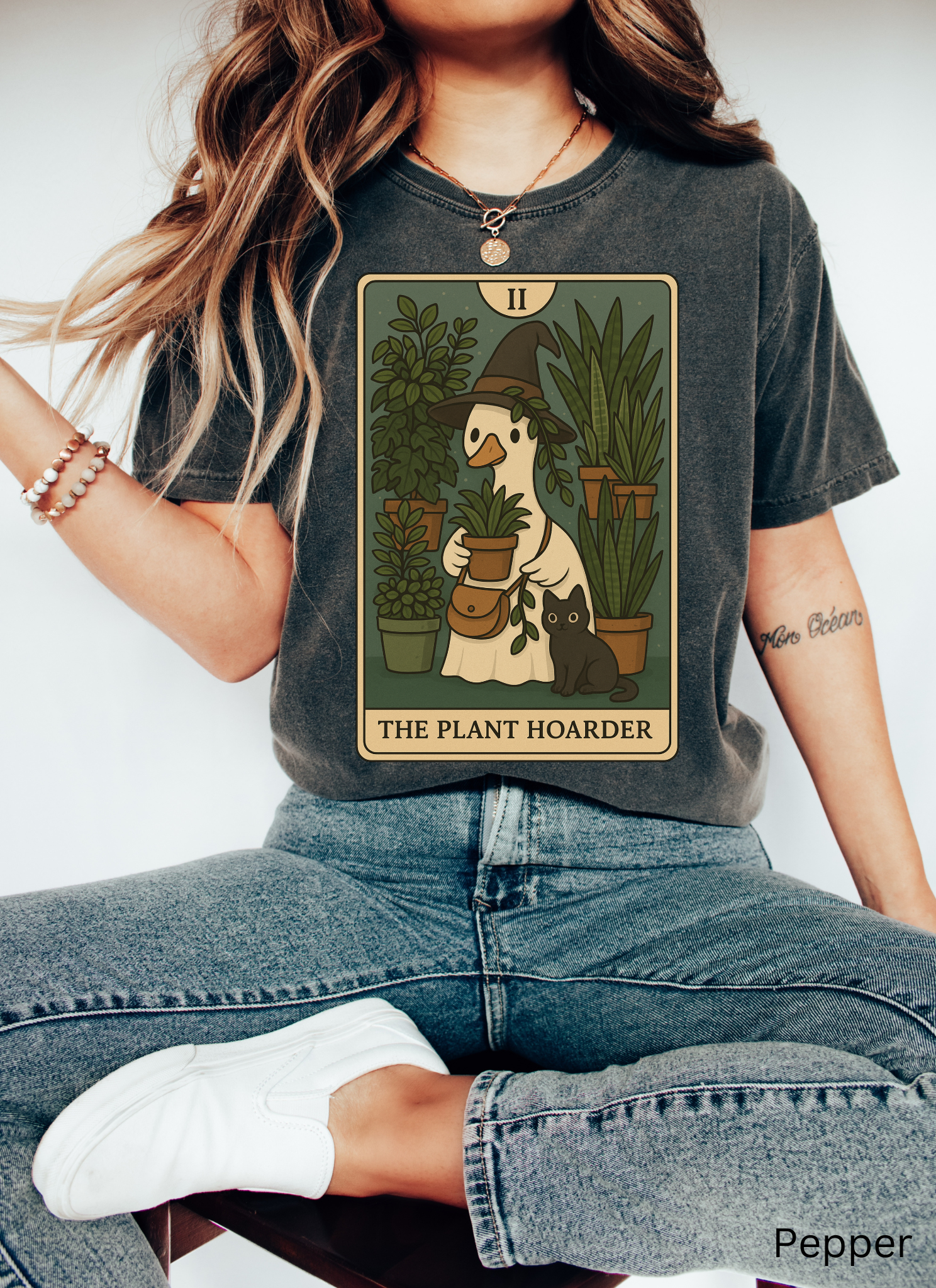 Witchy plant hoarder shirt featuring a tarot card design of a goose in a witch hat holding plants, surrounded by greenery and a black cat.
