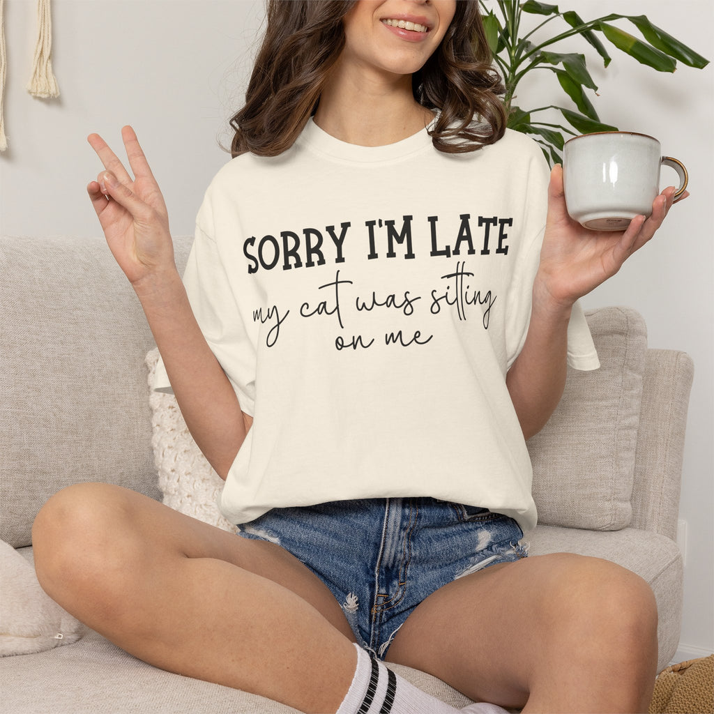 Funny cat lover graphic t-shirt featuring the quote "Sorry I'm Late My Cat Was Sitting on Me." A humorous gift for cat moms, cat dads, and anyone owned by a sleepy cat.